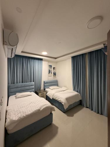 two beds in a room with blue curtains at Taqah Beach Front Apartment in Ţāqah