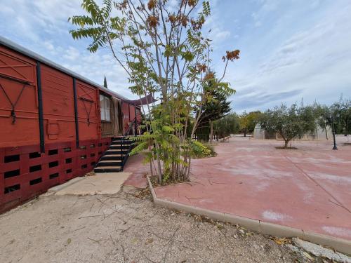a small tree next to a red building at Vagón con sesión de Jacuzzi in Caravaca de la Cruz