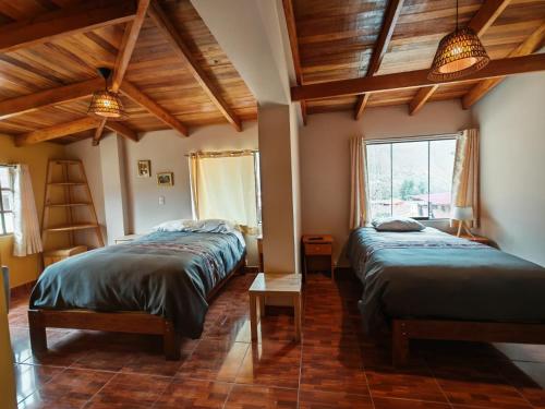 two beds in a room with wooden ceilings and a window at Sunshine in Ollantaytambo