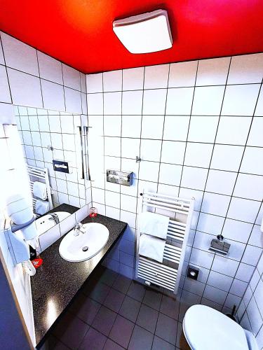 a bathroom with a sink and a toilet and a red ceiling at Ibis Vienna Airport in Schwechat