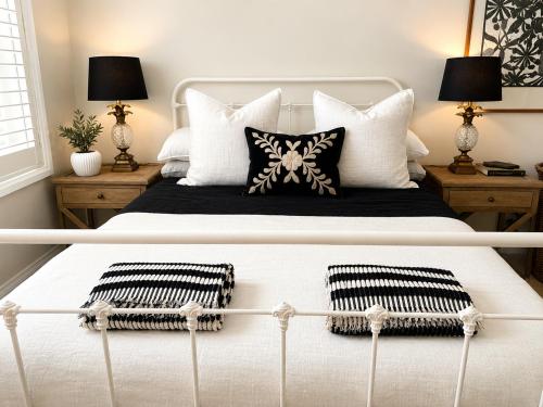 a bedroom with a white bed with black and white pillows at Avalon Beach Cottage- The Islander in Avalon
