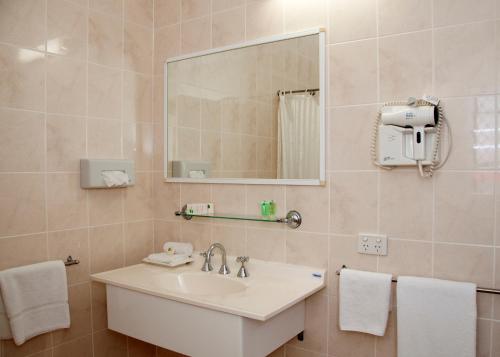 ein Badezimmer mit einem Waschbecken, einem Spiegel und Handtüchern in der Unterkunft Jackaroo Motel in Mareeba