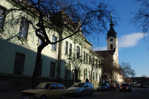 a building with a clock tower and cars parked on the street at Apartman Milkovic 2 in Sombor
