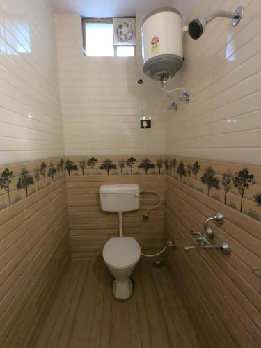 a bathroom with a toilet in a room with trees on the wall at Bagwan Kainchi Stay in Bhowāli