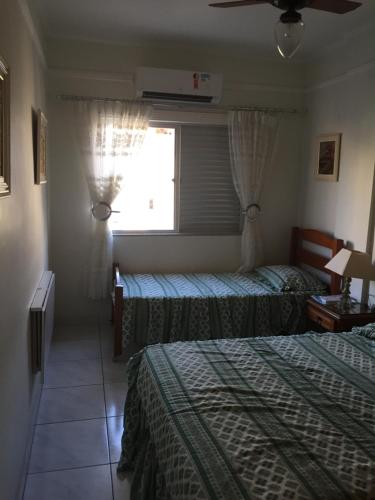 a hotel room with two beds and a window at Apartamento Astúrias 2 Dorms Ar Cond in Guarujá