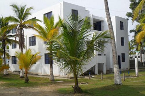 a white building with palm trees in front of it at Apartamentos Las Múcuras in Coveñas