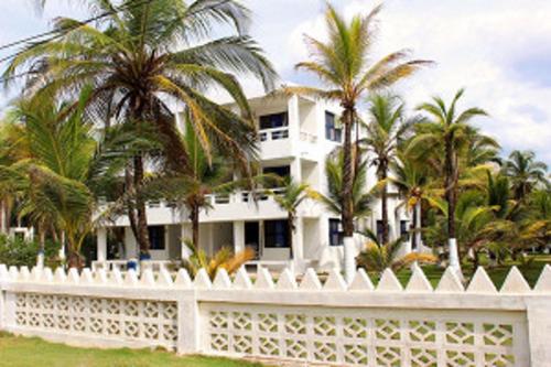 a white house with palm trees behind a white fence at Apartamentos Las Múcuras in Coveñas