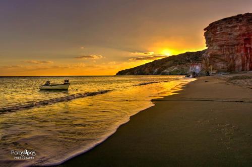 a boat in the water on a beach at sunset at Semiramis Guesthouse in Adamas