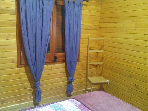 a bedroom with blue curtains and a chair and a window at Casa dos Manos in Furnas