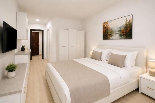 a white bedroom with a large bed and a tv at Nicolle Prestige Apartment in Piteşti