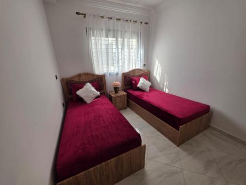two beds with red sheets in a room with a window at Appartement sur Mer in El Arba de Trougout