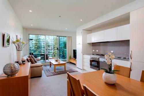 eine Küche und ein Wohnzimmer mit einem Tisch und einem Sofa in der Unterkunft Glenelg Holiday Apartments-Pier in Adelaide