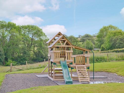 a wooden play structure with a slide and a playground at The Stable - Om4 in Mydroilin