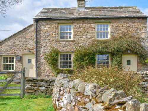 an old stone house with a stone wall at Alpine Cottage in Carperby