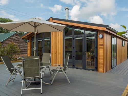 a deck with chairs and an umbrella and a house at Oak Lodge in Hassocks