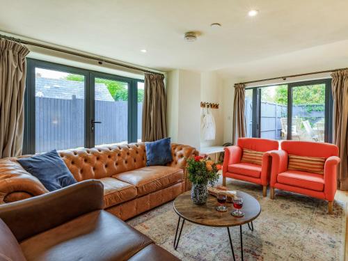 a living room with a brown couch and two red chairs at Coach House - Uk32202 in Burton Bradstock