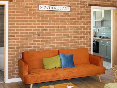 an orange couch against a brick wall with two pillows at No 8 Mouse Hole-Uk44302 in Sparham