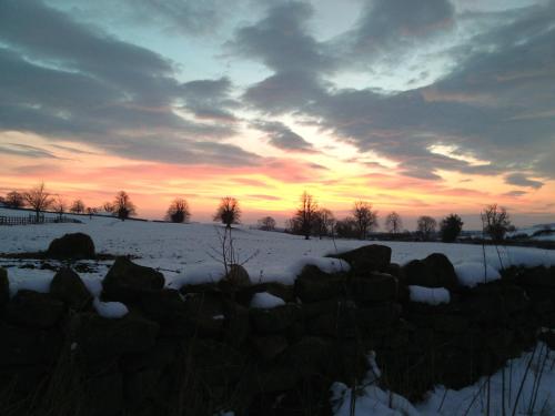 a fence in a snowy field with a sunset at Sykelands Cottage in Ravensworth