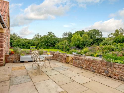 a patio with a table and chairs and a stone wall at The Stables in Cheddar