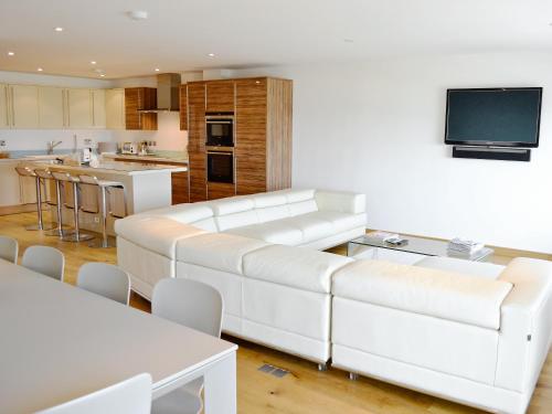 a living room with a white couch and a kitchen at Gylly Beach View - Tor in Falmouth
