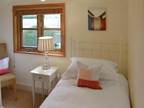 a bedroom with a bed with a lamp and a window at May Cottage in Bacton