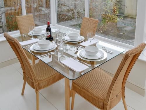 a glass table with chairs and a bottle of wine at May Cottage in Bacton
