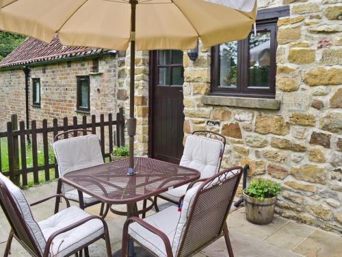 a patio with a table and chairs and an umbrella at Paper Mill Cottage in Sutton