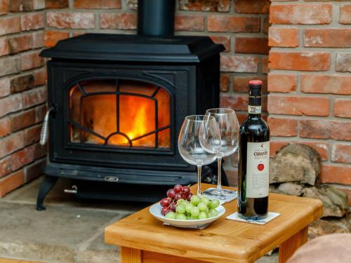 a bottle of wine and wine glasses on a table with a fireplace at The Old Laundry - Uk12136 in Hewelsfield
