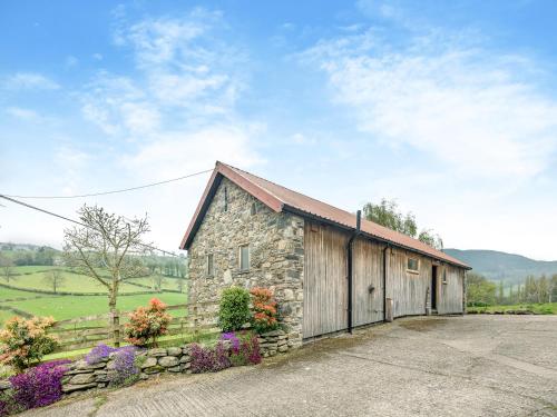 a stone barn with a fence and flowers at Wern Ddu Cottage in Pen-y-bont-fawr