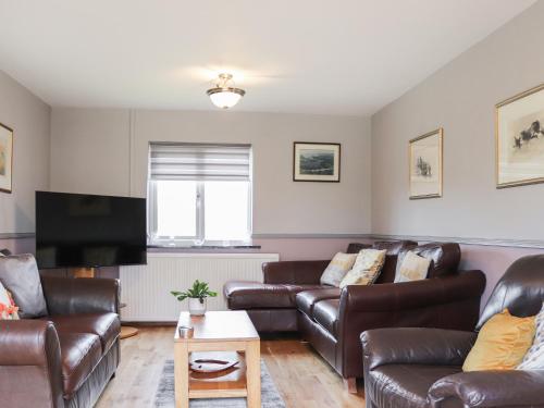 a living room with leather furniture and a flat screen tv at Ty'n Rallt in Bodorgan