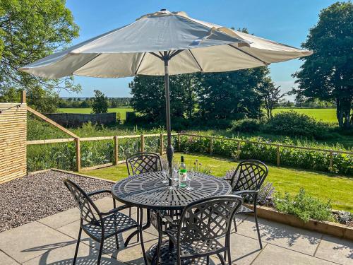 a table and chairs with an umbrella on a patio at Kingfisher Cottage in Kirkton of Airlie