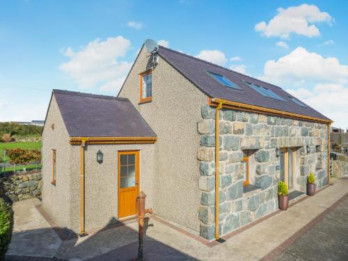 a stone house with a yellow door and windows at Deri Cottage in Chwilog