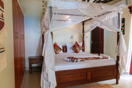 a bedroom with a canopy bed with white curtains at Tahira Villa in Diani Beach