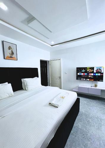 a bedroom with a large white bed with a tv on the wall at Auxano Apartments in Abuja