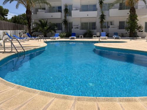 a large swimming pool with blue chairs and a building at Costamar 15 - Pool - 3 minutes to the beach in Es Pujols