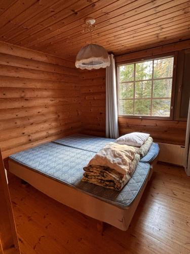 a bed in a log cabin with a window at Kalliorinteen Mökit Suvipirtti in Töysä