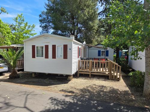 a small white tiny house with a wooden porch at Vias Plage - Camping Les Salisses - Mobilhome in Vias