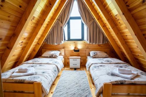 two beds in a log cabin bedroom with a window at Zov planine in Žabljak