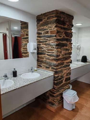a bathroom with two sinks and a stone wall at O Solpor Fillobal in Vilar