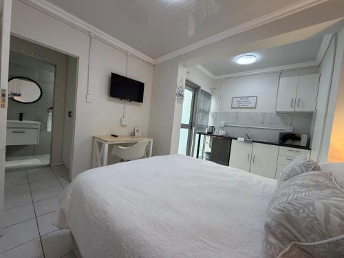 a white bedroom with a large bed and a kitchen at The Ceed in Beacon Bay