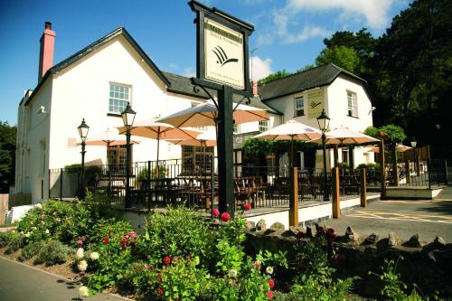 a clock in front of a building with tables and umbrellas at The Malvern Hills Hotel in Great Malvern