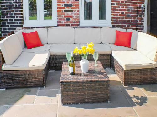 a patio with two couches and a table with flowers at Holly Barn in Ashwellthorpe
