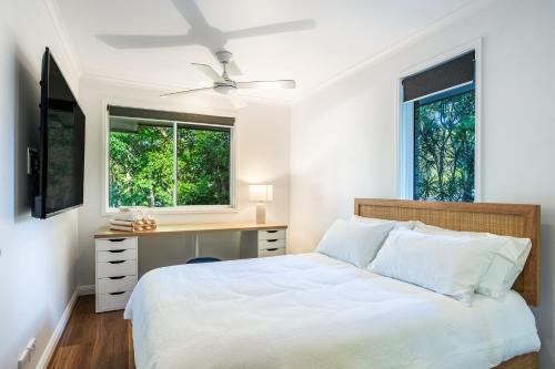 a bedroom with a bed and a desk and two windows at Treetops Sunrise Beach in Byron Bay