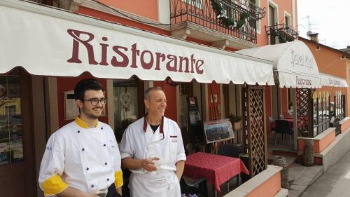 Dos hombres de pie frente a un restaurante en Hotel Alpi - Foza, en Foza