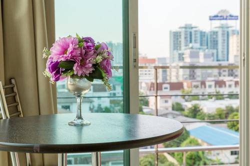 a vase of flowers sitting on a table in front of a window at Right Place Sathorn in Bangkok