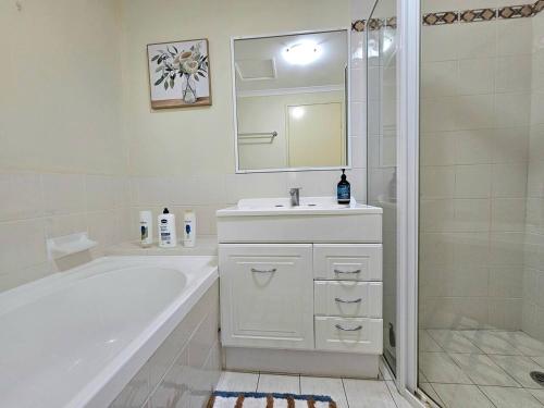 a white bathroom with a tub and a sink and a shower at Toukley Waterfront Apartment with Balcony - Outdoor Pool - Secure Parking - Wi-Fi - By HappyHosts in Toukley