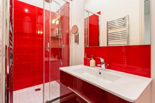 La salle de bains rouge est pourvue d'un lavabo et d'une douche. dans l'établissement Le Logis de Montmartre, à Paris