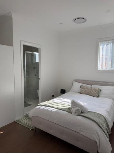 a white bedroom with a bed and a walk in shower at Second Home - A modern 4 Bedrooms House in Blacktown