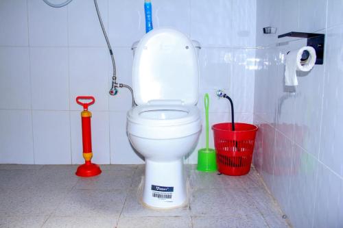 a bathroom with a white toilet and a red bucket at Tenzi BnB in Jinja
