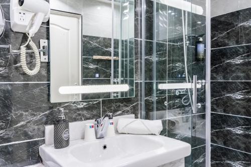 a black tiled bathroom with a sink and a mirror at HOTEL ROYAL Paris Ivry in Ivry-sur-Seine